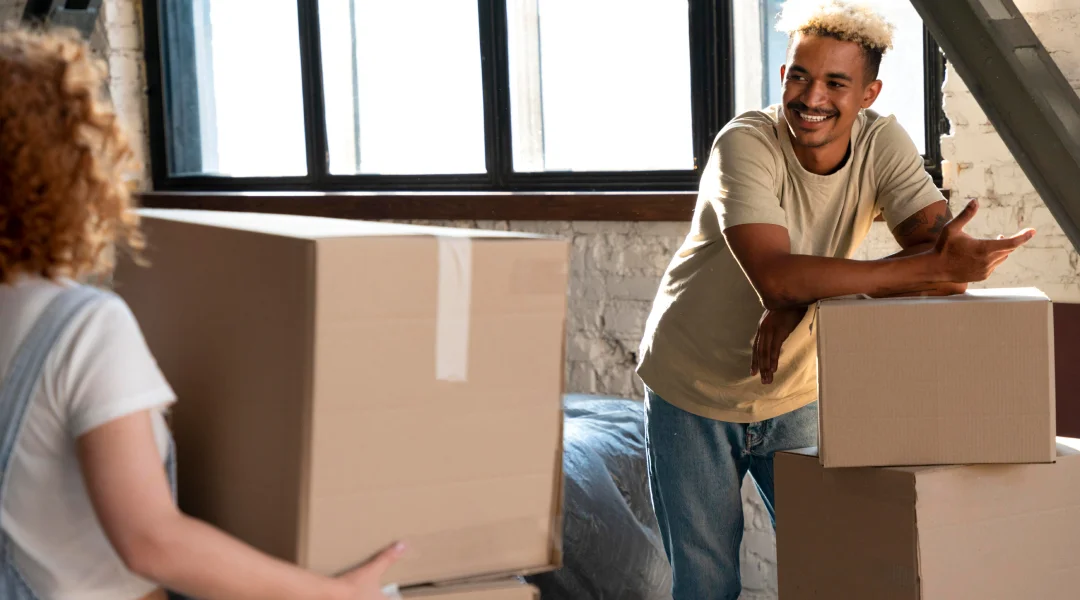 Un homme et une femme déplacent des cartons dans une pièce, illustrant un déménagement réussi.