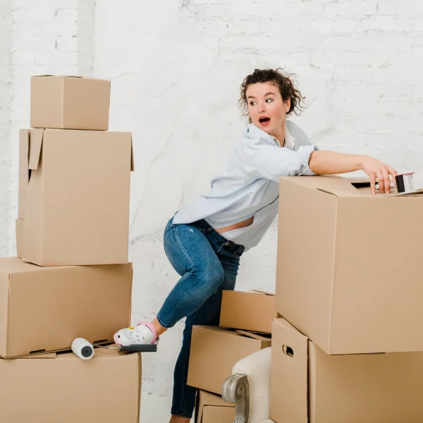 Une femme se tient devant une pile de cartons, illustrant les erreurs à éviter lors d’un déménagement.