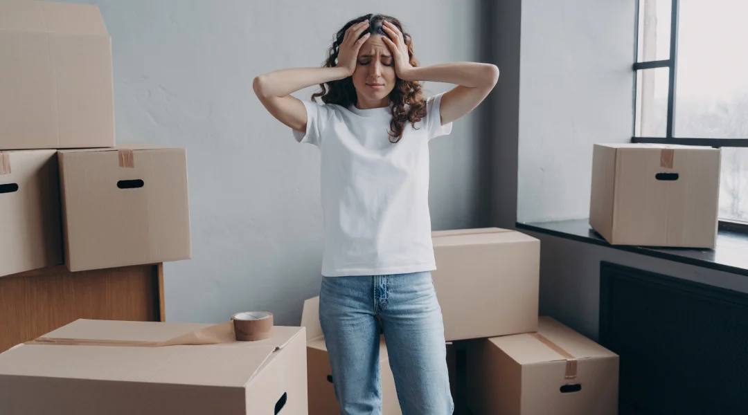 Une femme se tient devant des cartons, la tête dans les mains, exprimant du stress lié à un déménagement.